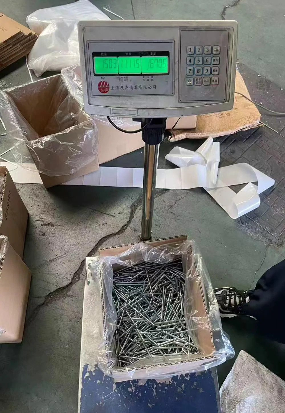 Long countersunk screw components in a carton beside a weighing scale during packing